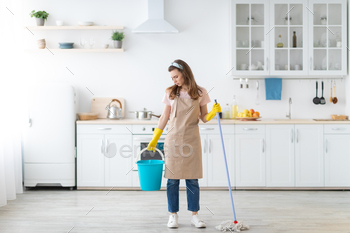 Full length portrait of upset millennial lady with mop and bucket unwilling to wash floor in kitchen / Photodune, Misc
