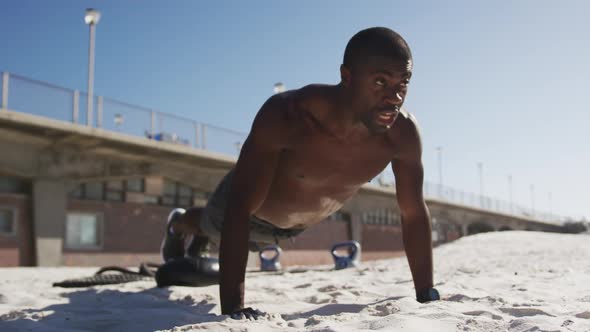 Focused african american man doing press ups, exercising outdoors on beach