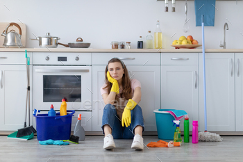 Exhausted young housewife sitting on floor at kitchen, surrounded by cleaning supplies, tired from / Photodune, Misc