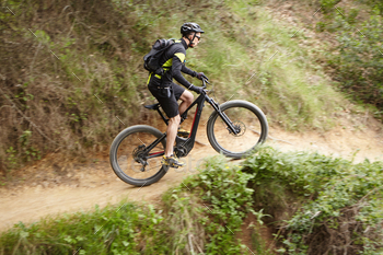 tain biking stunts on two-wheeled motor-powered bicycle on trail along cliff using pedal-assist system. Male biker cycling outdoors on electric bike