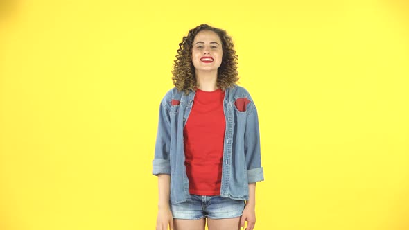 Young Curly Girl Shows Two Fingers Victory Gesture on Yellow Background at Studio