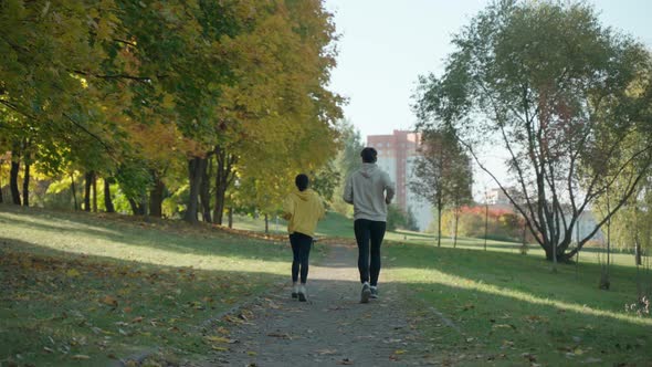 Young Man and Woman Running on a Track at the Park in Sunny Autumn Morning