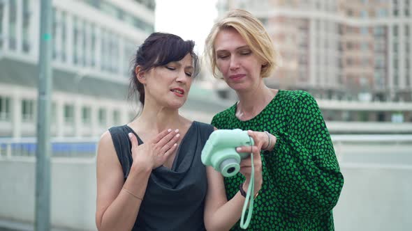 Adult Woman Admiring Talent of Friend Looking Through Photos on Camera Standing Outdoors