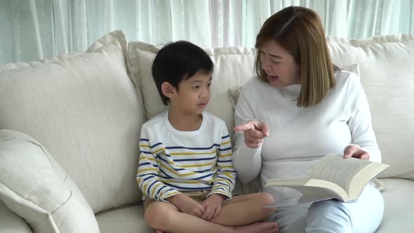 Asian Mother And Her Son Reading A Book On Sofa In Living Room Slow Motion 