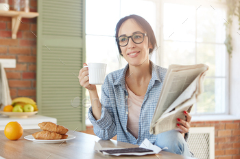  tea with croissants and chocolate, reads newspaper alone at home. Morning routine concept. Woman finds out news from local magazine during lunch