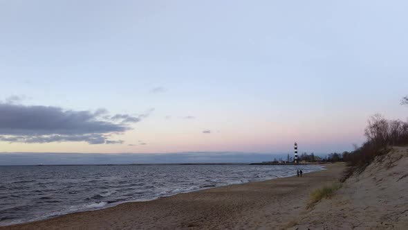 People walking near the sea during sunset. Lighthouse in background.