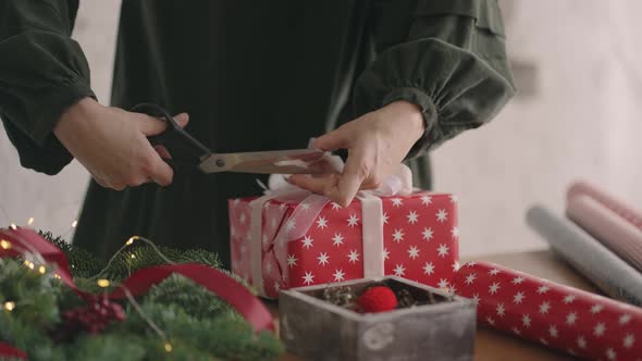 Closeup of a Woman Decorator with Scissors Cuts and Trims the Ribbon on the Packaging of a Gift for