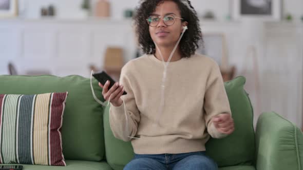 Young African Woman Listening To Music on Smartphone on Sofa