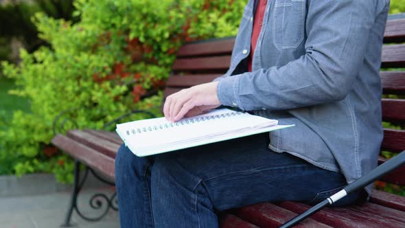 Blind Man Reading Braille Book Sitting on Bench in Summer Park