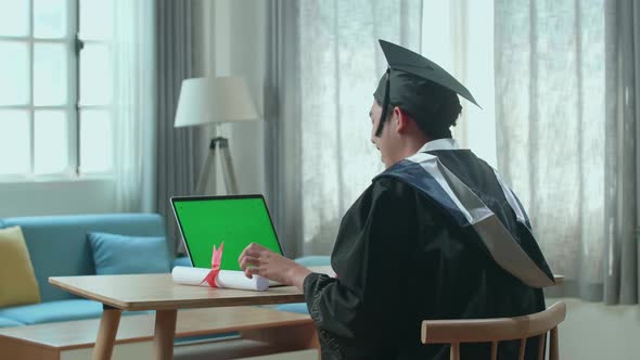 Excited Asian Man Showing Off A University Certificate To Laptop Computer With Green Screen