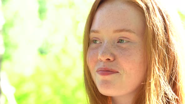 Portrait a Smiling Young Woman with Red Hair and Freckles Against the Backdrop of a Bright Sunny