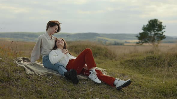 Two Loving Lesbians Sitting in Embrace on Blanket Outdoors