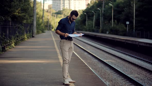 Businessman Tourist Looking On City Paper Map And Exploring City Route. Traveler Waiting Train.