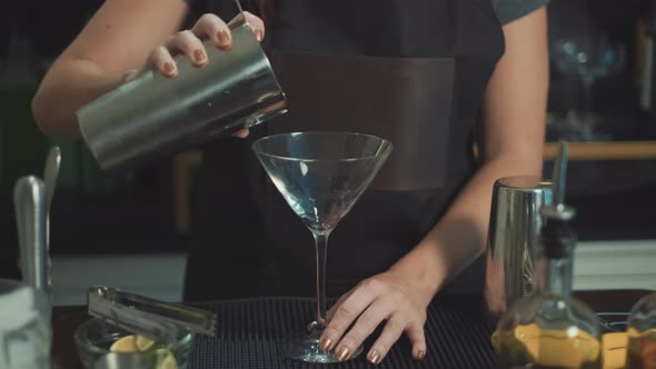 Mixologist pouring cosmo mixed drink into martini glass at speakeasy.