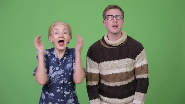 Grandmother Celebrating While Grandson Looking Upset Against Green Background