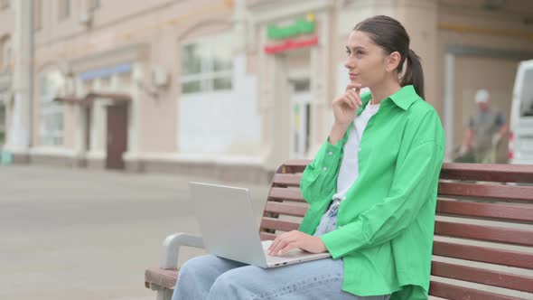 Thinking Hispanic Woman Using Laptop While Sitting Outdoor on Bench