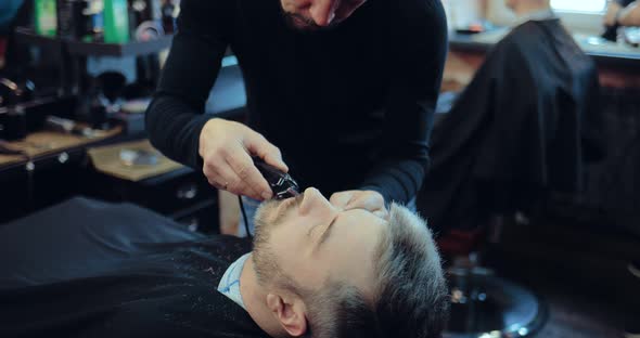 Man with Gray Hair Cuts His Beard in a Brutal Barber Shop