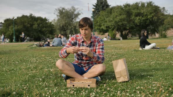 Man Opens Cardboard Box and Smells Pizza Sitting on Grass
