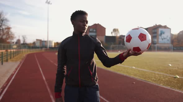 A Young Black Girl in Sportswear Stands at the City Stadium and Holds a Soccer Ball in Her Hand and