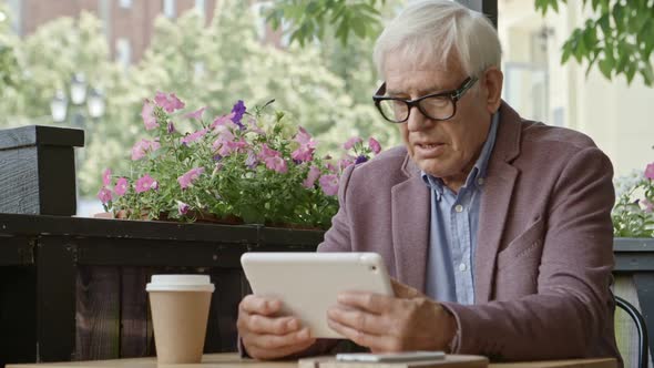 Senior Businessman Working on Tablet Over Coffee in Outdoor Restaurant