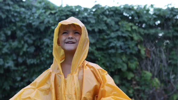 A Little Boy Stands in the Rain in a Raincoat