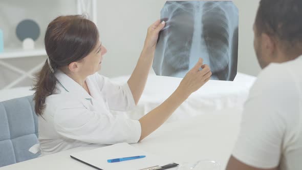 Doctor and Patient Examining Lungs X-ray in Hospital. African American Man and Caucasian Woman