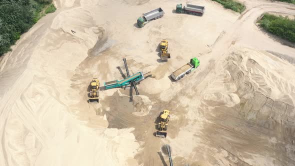 Top aerial view of bulldozer loading sand into empty dump truck in open air quarry.