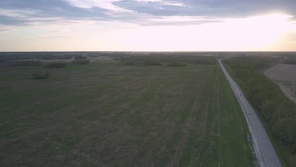 Wide Green Unharvested Field and Long Highway Against Forest