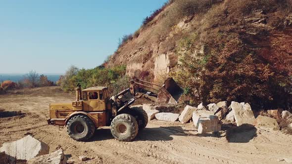 professional yellow bulldozer is working near sand quarry on the background of stones.