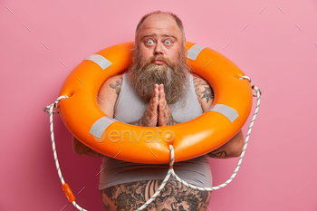 essed together and asks for help learns how to swim poses with inflated swim ring has thick beard tattooed belly isolated on rosy background