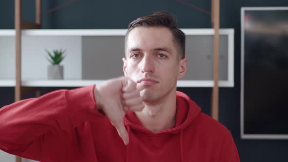 Dissatisfied Confused Young Millennial Man in Red Hoodie Tshirt Showing Thumb Down