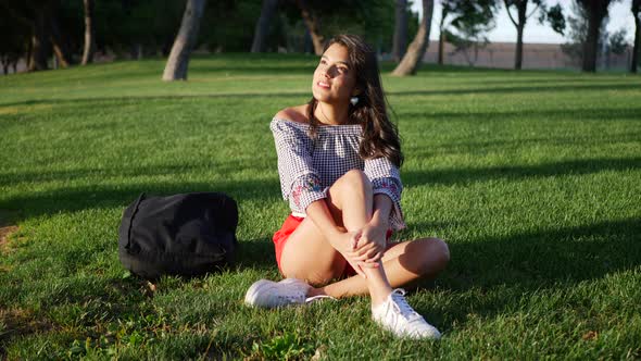 Beautiful young hispanic college student resting on a grassy park field between classes on campus.