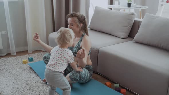 Happy Mindful Mother Doing Morning Exercises in Yoga Pose While Kid Daughter Playing at Home