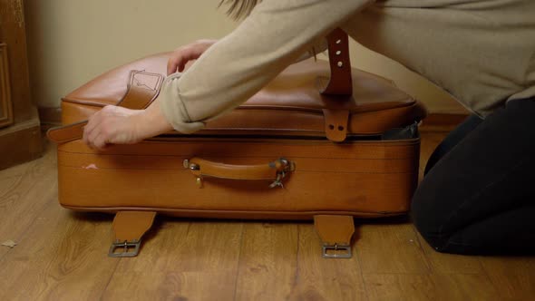 Woman unzipping old brown suitcase wide shot