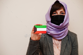 , protect face mask and hijab head scarf, hold Kuwait flag card against isolated background. Coronavirus country concept.