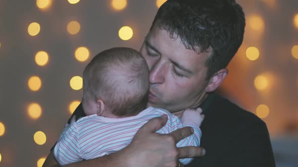 A Father Kisses His Child in His Arms at the Evening Lights