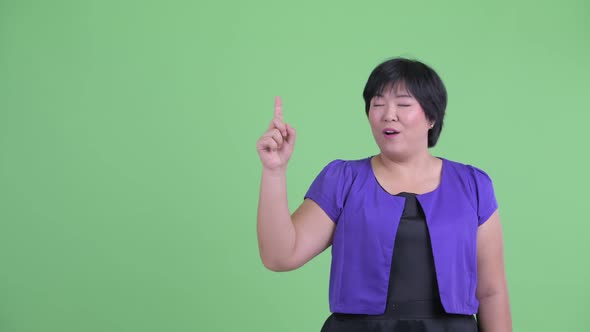 Happy Young Overweight Asian Woman Pointing Up and Looking Surprised