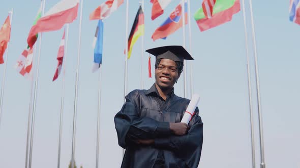 Happy Young African American Male Graduate Standing in Front of the Camera with a Diploma in His
