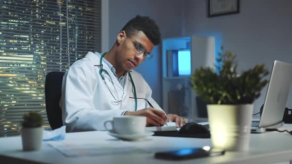 Mixedrace Doctor Making Notes and Talking By Video Call on Computer