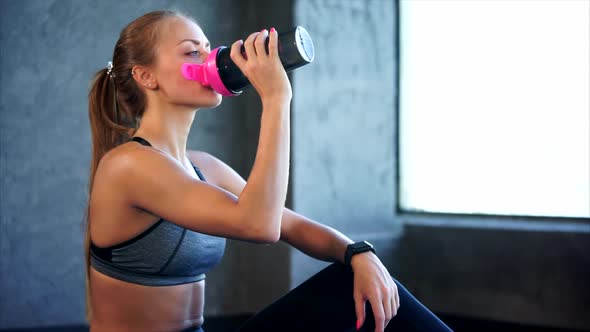 Beautiful Girl in Sport Clothes Drinking Water After Workout in the Gym.