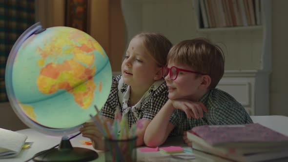 Schoolgirl and Schoolboy Studying Earth Globe on the Desk with Textbooks