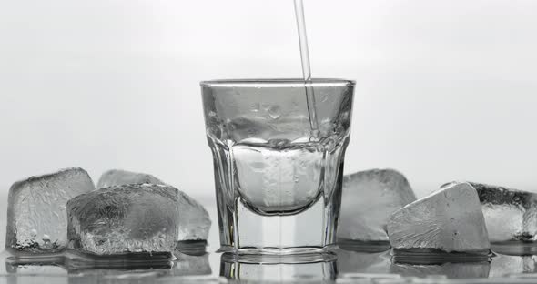 Pouring Up Shot of Vodka From a Bottle Into Glass. White Background