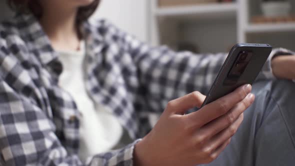 Faceless Woman Using Smart Phone In Home Room. Girl Using Smartphone, Sitting Near Shelves Using App