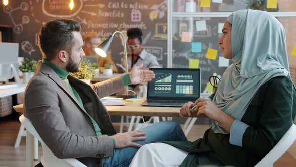 Caucasian Businessman and Mixed Race Muslim Businesswoman Talking Looking at Laptop Screen in Office