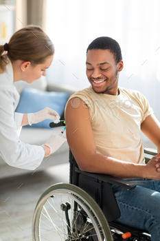 Young nurse administering covid-19 vaccine shot to black male handicapped patient in wheelchair / Photodune, Misc