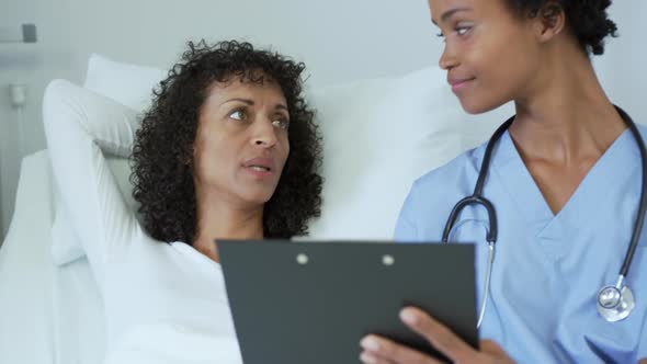Front view of African american female doctor talking with female patient in the ward at hospital