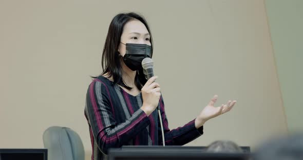 Asian Female Professor With Face Mask Explains To University Student In Classroom.