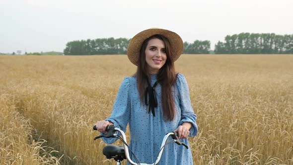 beautiful woman in straw hat dress is walking through wheat field with Bicycle