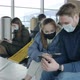 A Young Couple of Tourists in Protective Masks are Sitting in the Airport Lounge and Looking at the - VideoHive Item for Sale