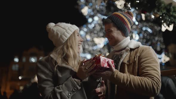 Man Presenting a Gift to His Girfriend at Square Celebrating Christmas